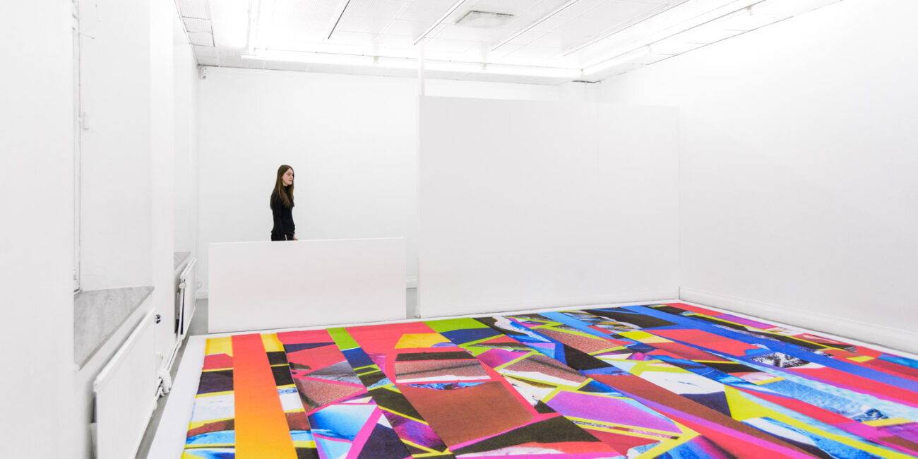 contemporary colorful carpet as an art installation by Stefano Conti in a white gallery, with a visitor.